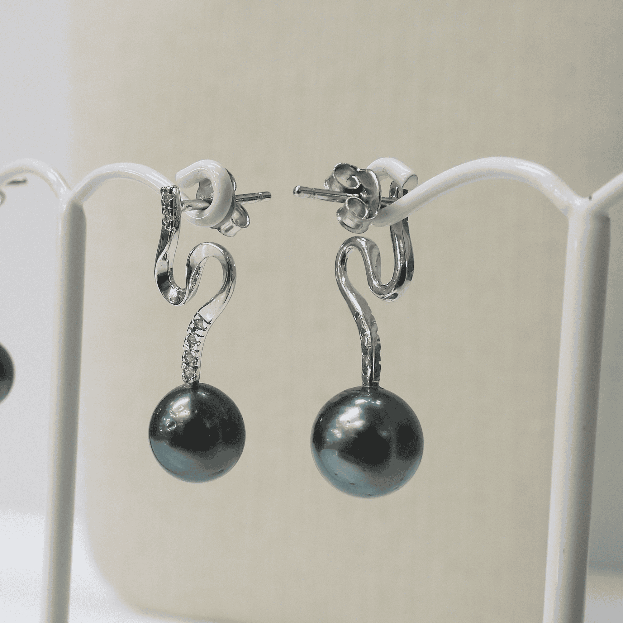 Shiny silver dangle earrings with black pearl accents, displayed on a white jewelry stand.